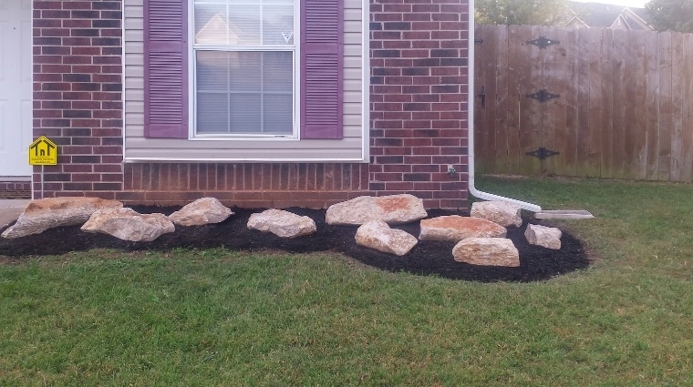 A large landscape bed lining a residential home filled with fresh black mulch and decorative rocks.